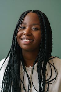 Close-up portrait of a cheerful young woman with braided hair against a green background.