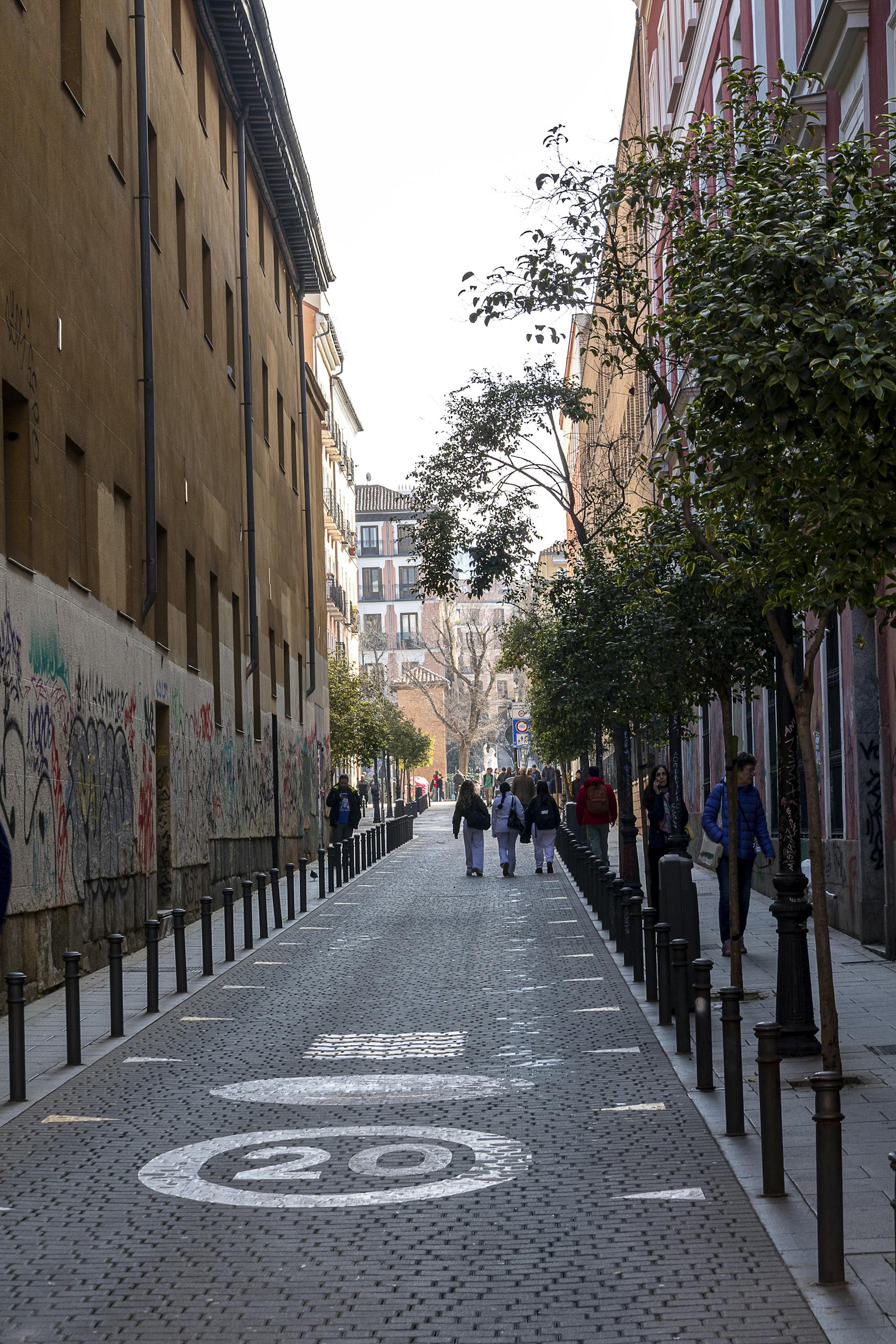 A lively street in Madrid's Barrio with people walking amidst charming architecture and urban art.