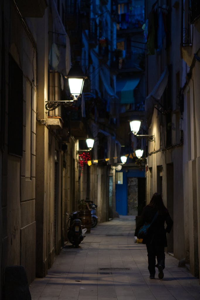 A shadowy narrow alley in Barcelona, illuminated by street lamps, captures a city's evening charm.