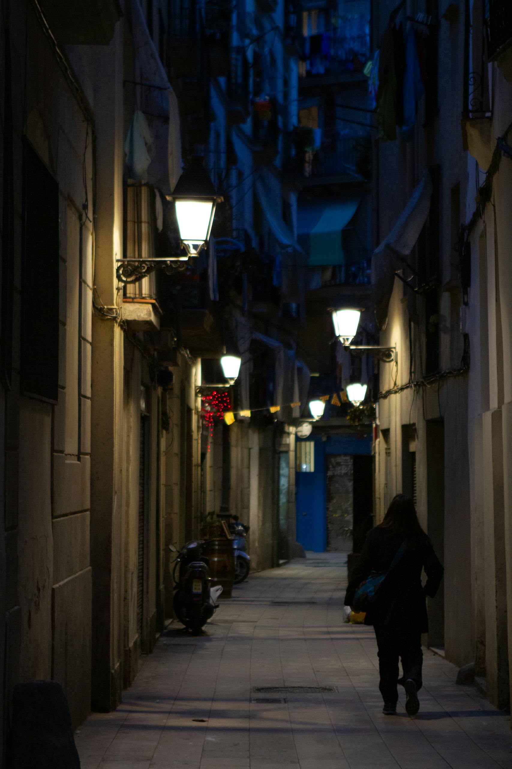 A shadowy narrow alley in Barcelona, illuminated by street lamps, captures a city's evening charm.